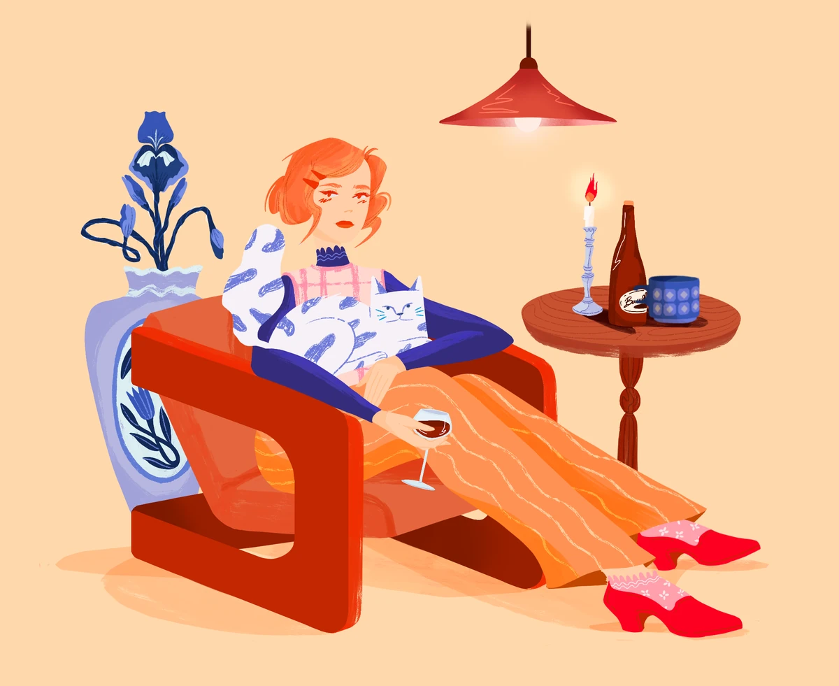 Red-haired woman relaxing in a red armchair with a glass of wine and a white cat on her lap